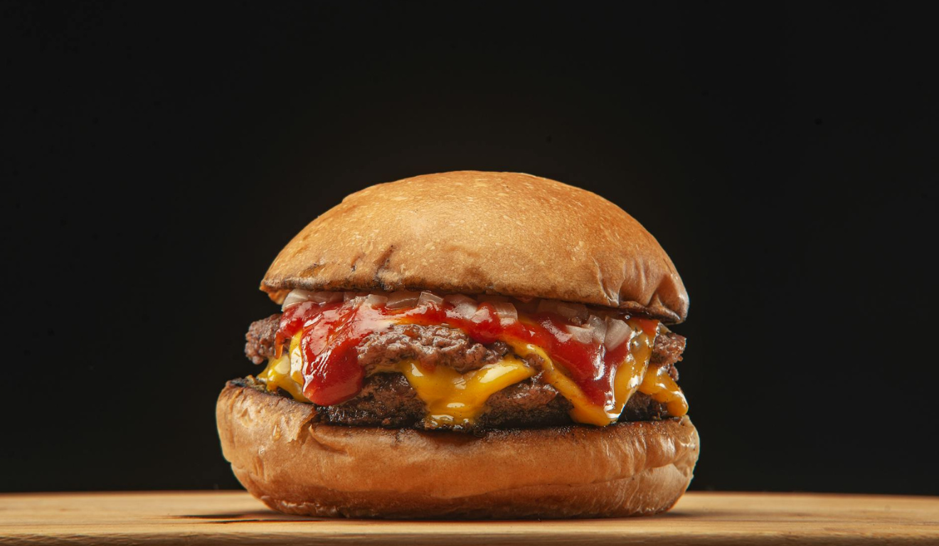 A imagem representa um hambúrguer feito com carne moída brasileira, afetada pelas tarifas norte-americanas, servido com queijo e pão artesanal