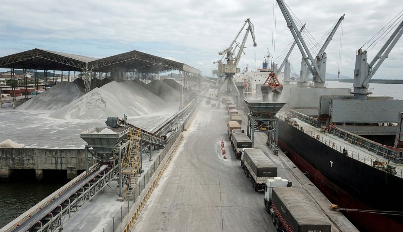 Vista aérea de operação logística de desembarque e movimentação de uma grande montanha de fertilizantes a granel em um porto brasileiro, ilustrando o volume recorde de importação em 2025. Vista aérea de operação logística de desembarque e movimentação de uma grande montanha de fertilizantes a granel em um porto brasileiro, ilustrando o volume recorde de importação em 2025.