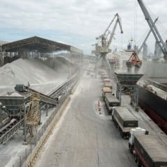 Vista a&eacute;rea de opera&ccedil;&atilde;o log&iacute;stica de desembarque e movimenta&ccedil;&atilde;o de uma grande montanha de fertilizantes a granel em um porto brasileiro, ilustrando o volume recorde de importa&ccedil;&atilde;o em 2025.