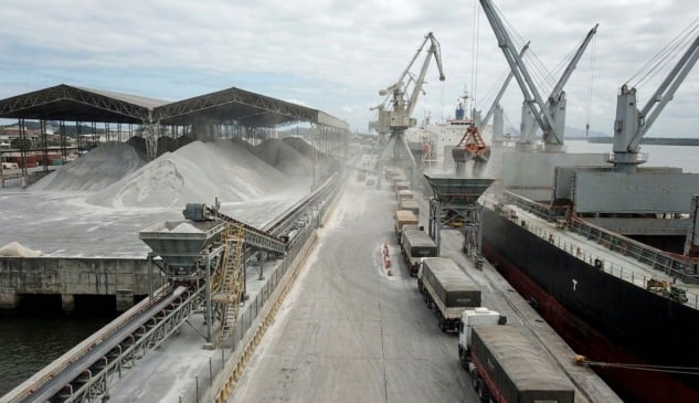 Vista aérea de operação logística de desembarque e movimentação de uma grande montanha de fertilizantes a granel em um porto brasileiro, ilustrando o volume recorde de importação em 2025.